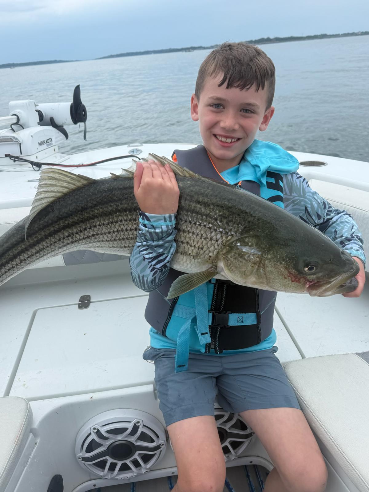 Young angler holding a big striped bass on the bay